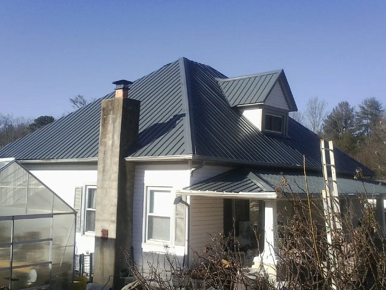 Dark blue standing seam metal roof on a white farmhouse with dormer in Northville