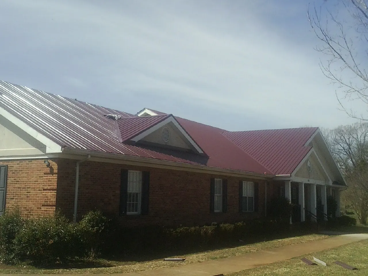 Red metal roof with gabled entries on a long brick building, from a Hail Damage Roof Repair job in Northville