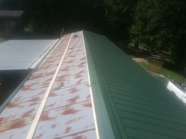 Old rusted panels beside newly installed green metal roofing — Wind Damage Roof Repair by Roofing Brothers in Northville