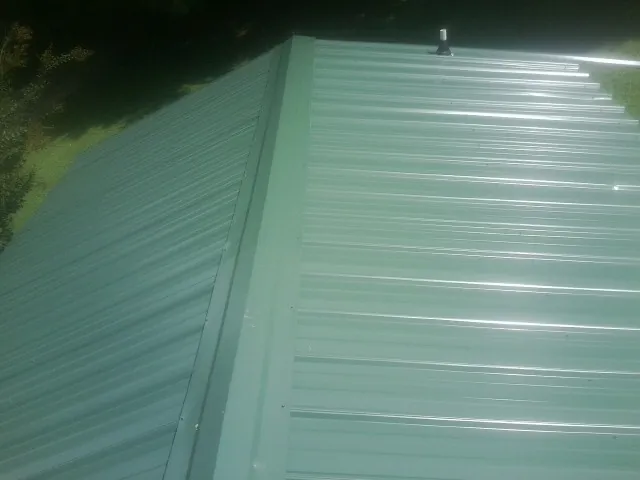 New green metal panels meeting at the ridge of a roof — Flat Roof Repair work by our crew in Northville