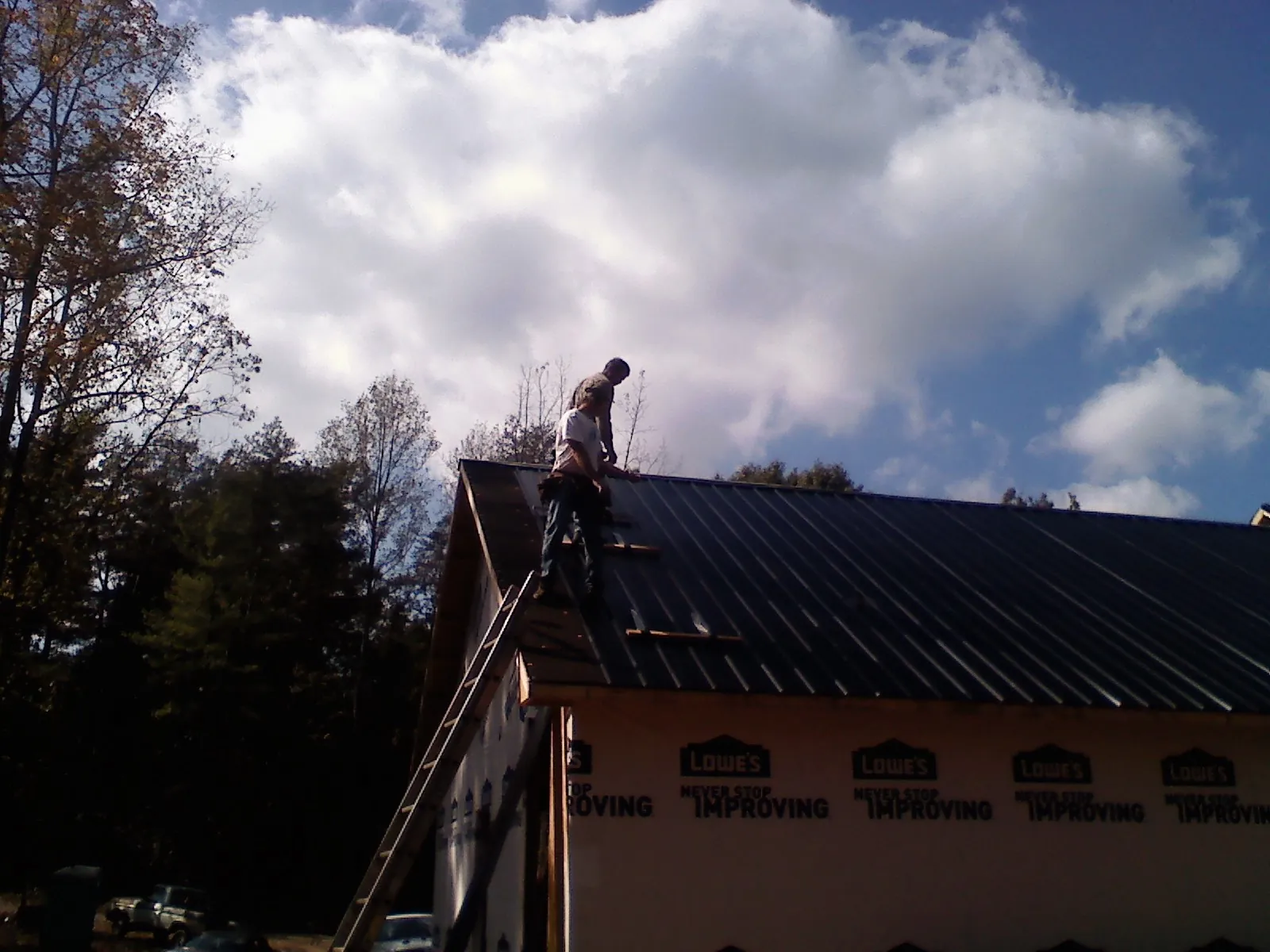 Roofer fastening dark metal panels high against a cloudy sky, from a Roof Inspection job in Northville