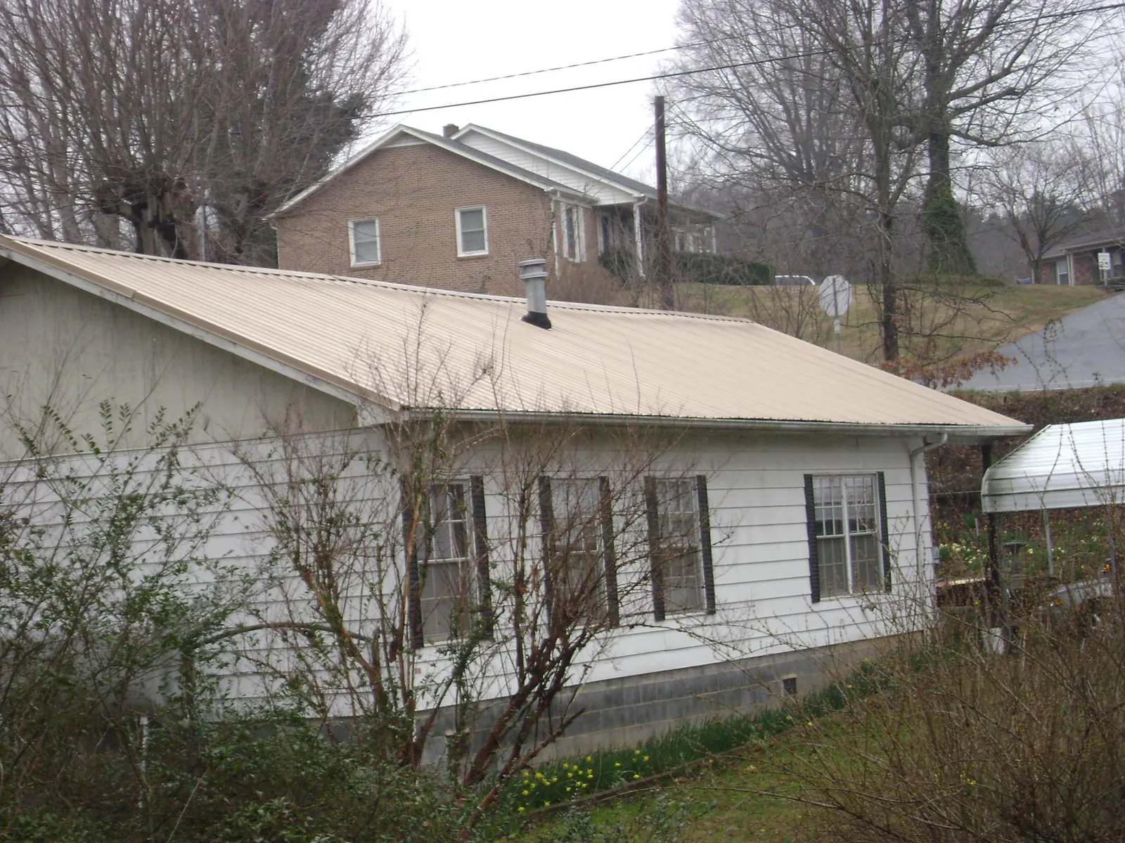 Tan metal roof on a white sided house set into a hillside — Commercial Roofing by Roofing Brothers in Northville